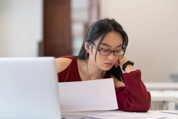 Hårt arbetande asiatisk student flicka i glaser läsa arkitektoniska ritningar medan du studerar i biblioteket — Stockfoto