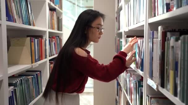 Japans student meisje op zoek naar boek in universiteitsbibliotheek plukken roman of materiaal voor cursus werk — Stockvideo