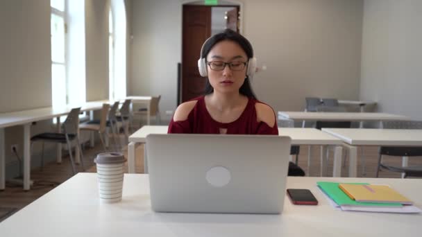 Fiatal ázsiai nő szabadúszó fülhallgató munka gépelés laptop számítógép ülni íróasztal nyitott irodában — Stock videók