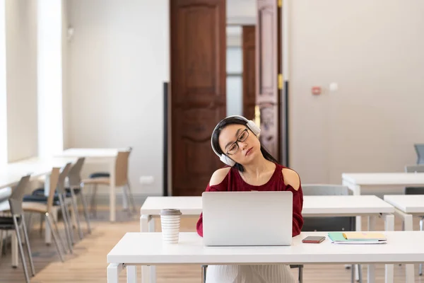 Trött asiatisk student flicka i hörlurar som gör gymnastik medan du studerar online i moderna klassrum — Stockfoto