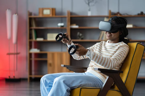 Happy young african american woman wearing virtual reality goggles playing video games at home — Stock Photo, Image