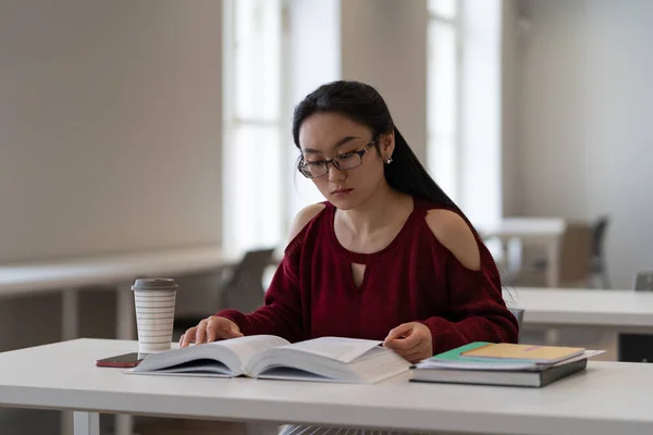 Nerdy aziatische meisje het lezen van leerboek tijdens de voorbereiding van examen of test in de bibliotheek leeszaal — Stockfoto