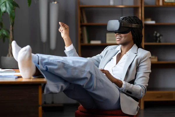 Curious afro businesswoman in vr goggles headset touching 3d virtual objects sit at office workplace — Stock Photo, Image