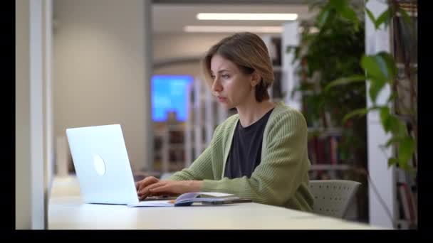 Töprengő skandináv nő tanul online laptopon hangulatos fény könyvtár sok növény — Stock videók