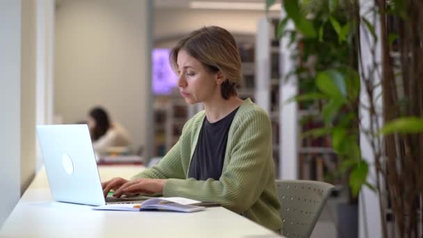 Koncentrerad kvinnlig universitetsprofessor kollar kursplan medan han sitter i tomt bibliotek — Stockvideo