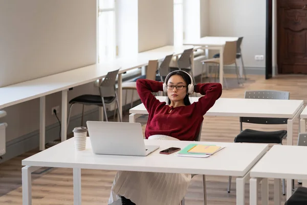 Jovem estudante asiática vestindo fones de ouvido estudando online na sala de leitura da biblioteca — Fotografia de Stock