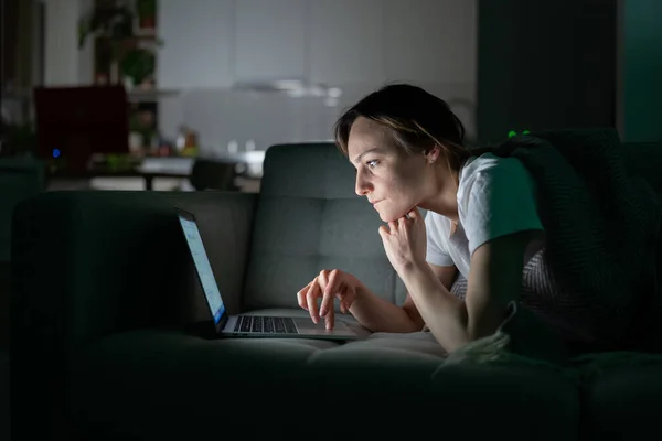 Soustředěná žena pracující online na notebooku doma v noci, dívající se na obrazovku, čtení zpráv. — Stock fotografie