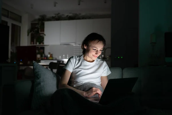 미소짓는 여성 프리랜서가 소파에 앉아 컴퓨터를 하고 밤에 집에서 비디오 통화를 하는 모습 — 스톡 사진