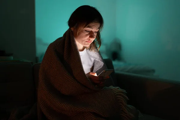Ospalá žena sedící na gauči pomocí chytrého telefonu pozdě v noci, nemůže spát. Nespavost, závislost. — Stock fotografie