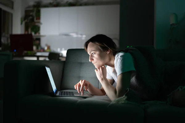 Soustředěná žena pracující online na notebooku doma v noci, dívající se na obrazovku, čtení zpráv. — Stock fotografie