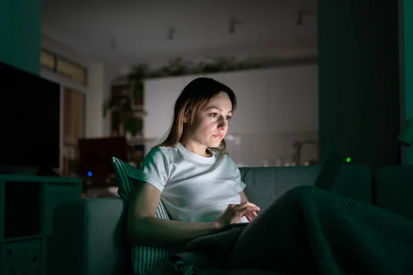 Zamyšlená mladá žena pracující na notebooku doma v noci, sledující vzdělávací video. — Stock fotografie