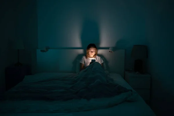 Mujer somnolienta acostada en la cama con teléfono inteligente tarde en la noche, no puede dormir. Insomnio, concepto de adicción — Foto de Stock