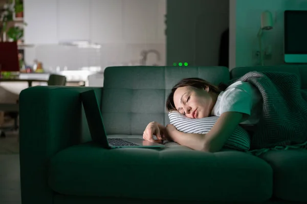 Giovane donna esausta che dorme sul divano dopo aver lavorato con il computer portatile a tarda notte a casa — Foto Stock
