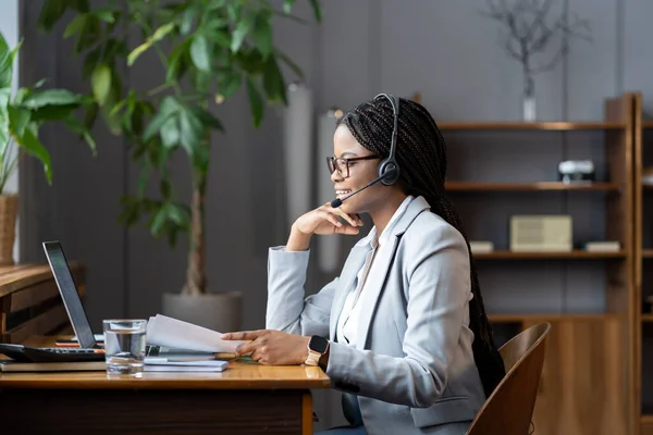 Jovem mulher africana positiva recrutador remoto usando fone de ouvido sem fio para se comunicar com os candidatos — Fotografia de Stock