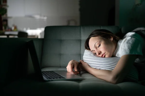 Vyčerpaná mladá žena spí na gauči po práci s notebookem pozdě v noci doma — Stock fotografie