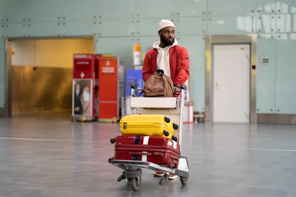 黒の男は空港ターミナルに到着した後、荷物トロリーウォーキングを押す。休暇、旅. — ストック写真