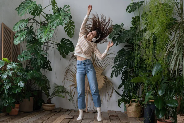 Mujer feliz usar auriculares inalámbricos escuchando música, bailando en el jardín casero con plantas tropicales — Foto de Stock