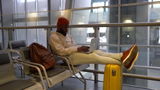Jonge hipster zwarte man zittend in luchthaven terminal werken op laptop wachten en landen aan boord. — Stockvideo