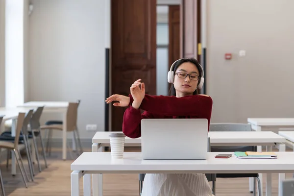 Menina asiática estudante esticar as mãos e assistir webinar para cursos distantes no laptop no espaço de co-trabalho — Fotografia de Stock