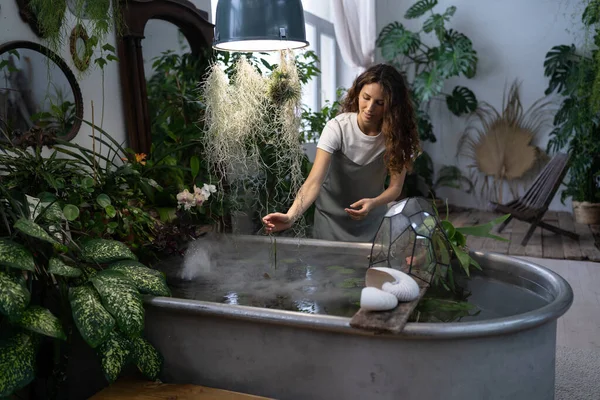 Девушка садовник заботиться о водном растении в оранжерее держа комнатное стекло под ванной с водой — стоковое фото