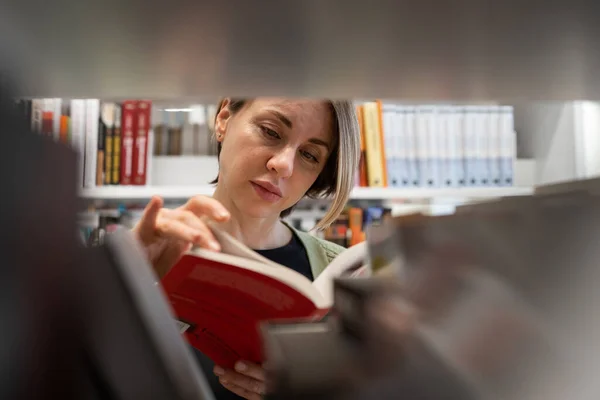 Vrouwelijke Volwassen Student Die Tussen Boekenplanken Universiteitsbibliotheek Staat Boek Uit — Stockfoto