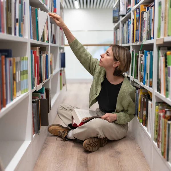 Pensive Woman Mature Student Sitting Cross Legged Library Floor Reaching — Stock fotografie