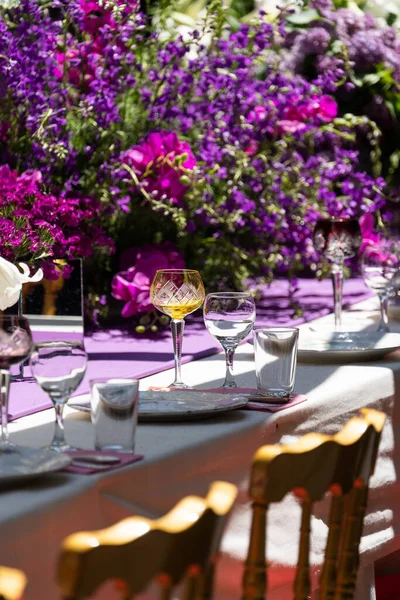 水晶和玻璃高脚杯和眼镜 白色盘子 节日餐桌的餐具 奢华婚礼或紫罗兰风格的生日宴会 用新鲜的紫色粉红花装饰 软焦点 — 图库照片