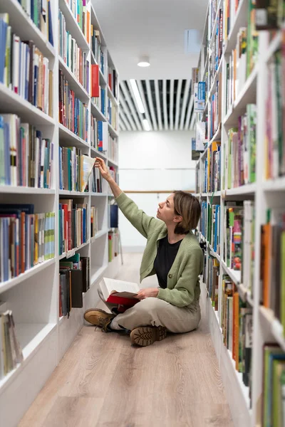 Interessato Femminile Seduto Gambe Incrociate Biblioteca Cerca Libri Alla Ricerca — Foto Stock