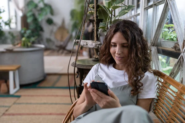 Glücklich Lächelnde Millennial Floristin Entspannen Gewächshaus Mädchen Halten Smartphone Sms — Stockfoto