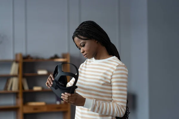 Interested excited black woman hold goggles for virtual reality simulation. Curious happy young woman with vr headset for making purchases in augmented reality store, playing games or watching 3d