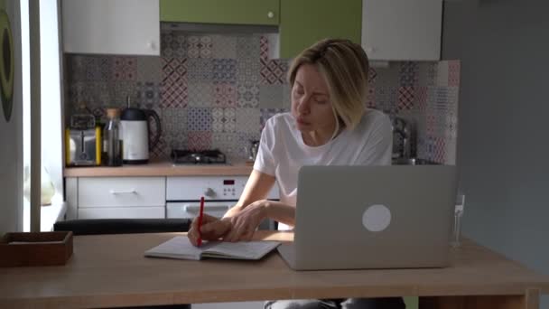 Сосредоточенная Женщина Средних Лет Сидит Дома Кухне Помощью Ноутбука Записывая — стоковое видео