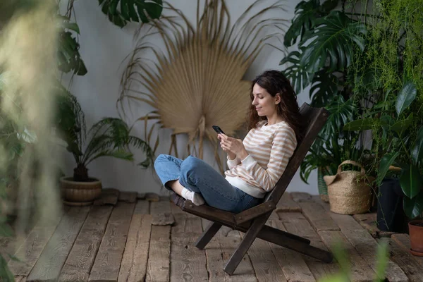 Radostná Mladá Žena Sedí Židli Útulné Botanické Zahradě Používá Smartphone — Stock fotografie