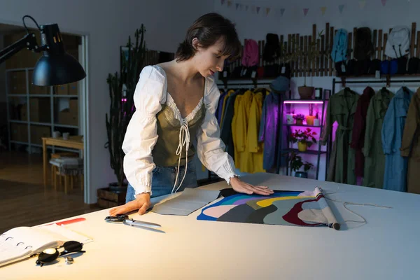 Woman dressmaker work late in studio choosing fabric samples for new clothes collection sewing. Female designer stay in workshop late busy with brand and small business development. Atelier ownership