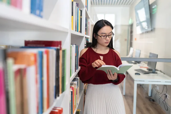 Asian student girl read book studying in modern library in university or college. Young female in eyeglasses prepare for exams in college or high school in academic public library. Education concept