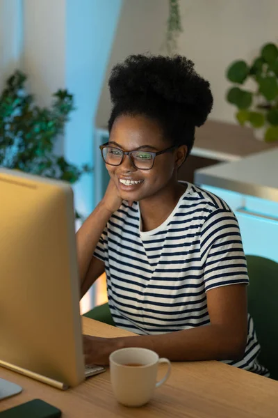 Happy African American female, successful remote web designer working on computer, joyful black woman freelancer earning money online, enjoying freelance life, soft focus. Remote work productivity