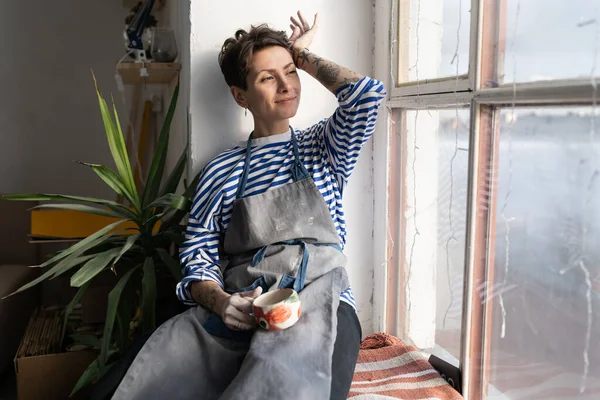 Pleased Young Georgian Woman Ceramist Apron Resting Studio Sits Windowsill — Stockfoto