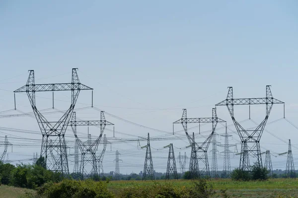 High-voltage lacy grid towers and power lines built in green field distribute electric energy against cloudy sky in countryside. Peak electricity consumption due to massive use of air conditioners
