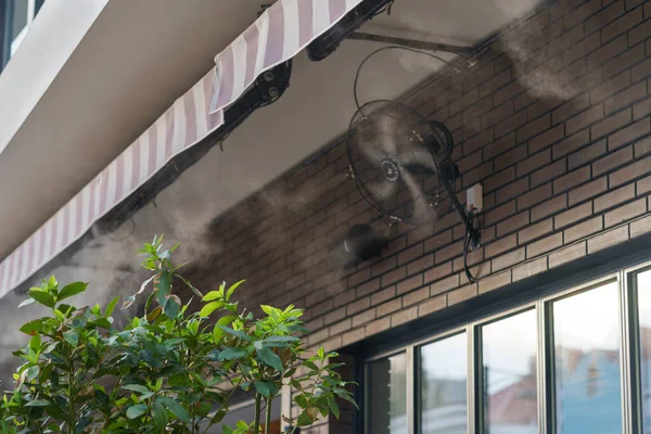 Water mist machine creates coolness on sunny day for comfort of visitors during heat and high temperature. Air cooling system with water vapor and fans on hot summer day for street cafe close view