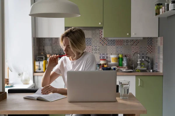 Σοβαρή Μεσήλικη Γυναίκα Κάθεται Ζεστή Κουζίνα Κάνοντας Σημειώσεις Χαρτί Σημειωματάριο — Φωτογραφία Αρχείου
