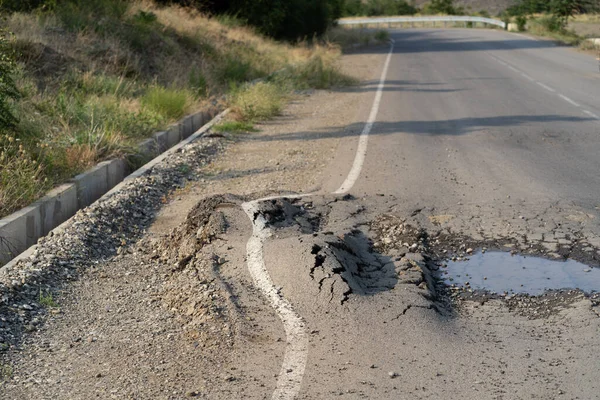 Deep hole in the road. Deformed asphalt surface with potholes melts from heat due to heavy overloaded trucks driving at hot summer days.