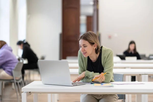 Online learning for adults. Pensive middle-aged woman studying on laptop in auditorium, using virtual learning platform. Mature female student engaged in study, watching webinar or attending e-class