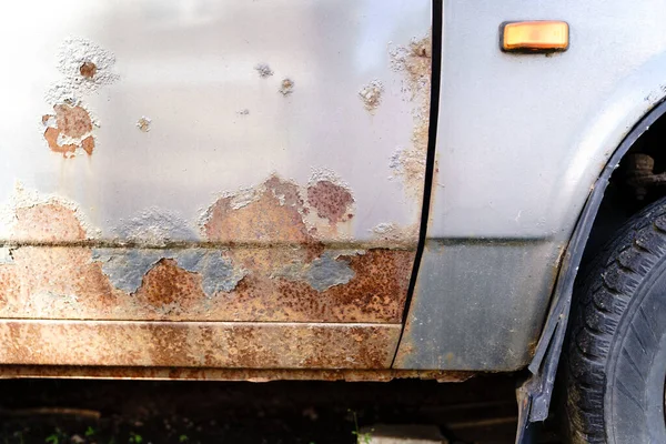 Damaged grunge dirty texture from road salt. Sheet metal corrosion of old silver vehicle. Rusty messy surface. Car door corrosion. Peeling paint.