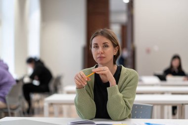 Mature students in higher education. Pensive middle-aged woman adult learner sitting at library table, preparing for exams, getting second degree, 45s female studying in classroom. Selective focus