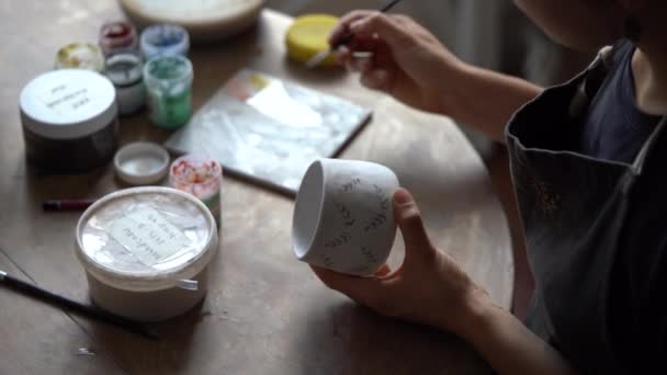 Focused Woman Paints Creative Pattern White Ceramic Cup Brush Sitting — стоковое видео