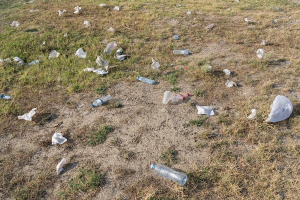 Rubbish from garbage dump spread by wind in rural area on summer day. Scattered plastic bottles and bags lie on grass in countryside causing pollution of environment. Ecological problem closeup view