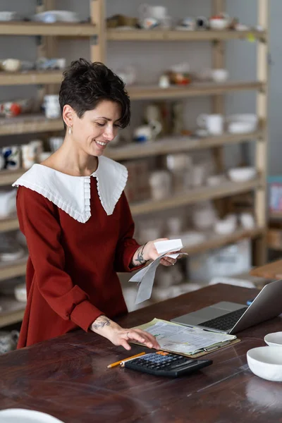 Happy Female Ceramist Pottery Studio Owner Holding Receipt Using Calculator — Zdjęcie stockowe