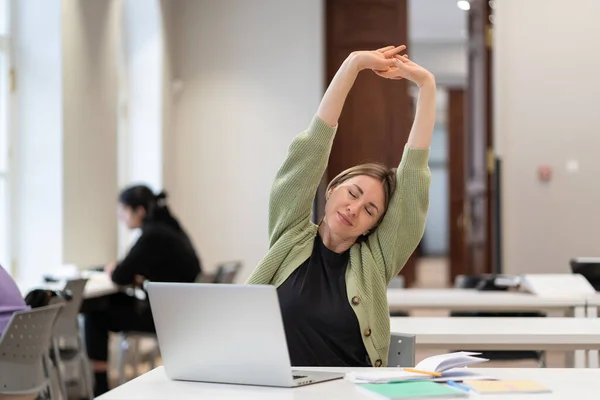 Happy middle aged female student warming up body and muscles at classroom, feeling satisfied with work done, smiling mature woman resting from computer screen. Education, happiness at work concept