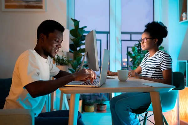 African American couple of freelancers works together at home. Black man and woman enjoy working together typing plans and information for articles about business project against potplants by window