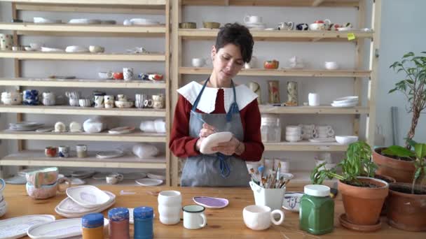 Femme Potier Concentrée Tenant Pinceau Peignant Sur Plaque Argile Atelier — Video