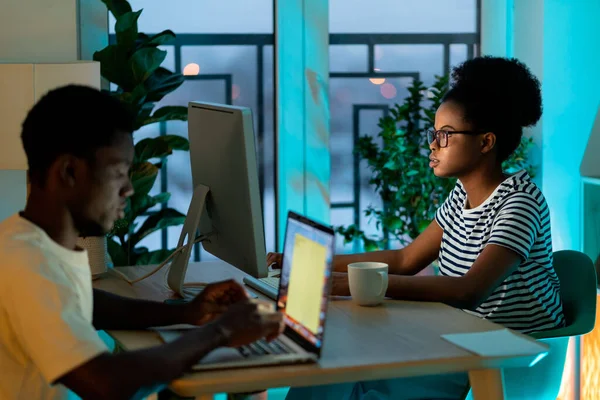 African American couple works freelancers at home sitting opposite at table. Black man and woman type important information for article about business project together against potplants by window